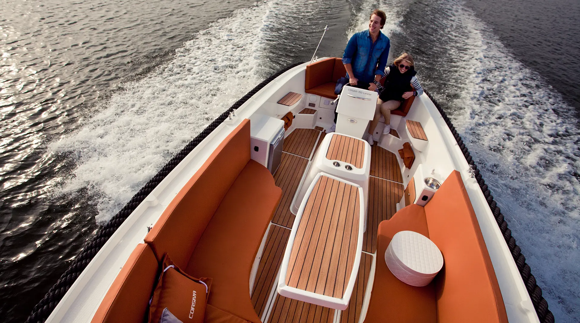Corsiva 700 Tender in Fahrt auf einem See, großzügiges Cockpit mit komfortablen Sitzbänken, Tisch und hochwertigem Teakoptik-Boden.