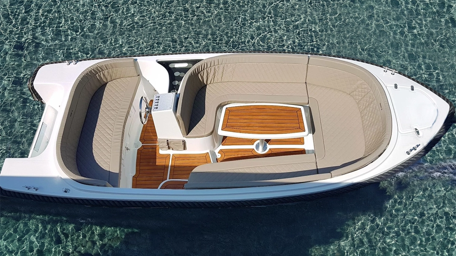 Draufsicht auf die Corsiva 520 New Age mit großzügiger U-Sitzgruppe, Tisch, Teakoptik-Boden und komfortablem Cockpit auf klarem Wasser.