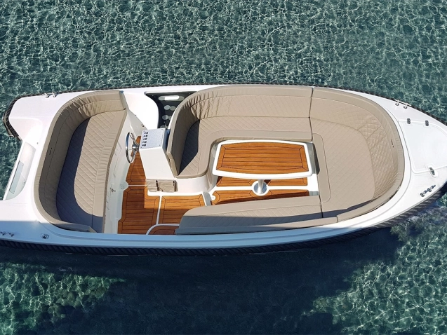 Draufsicht auf die Corsiva 520 New Age mit großzügiger U-Sitzgruppe, Tisch, Teakoptik-Boden und komfortablem Cockpit auf klarem Wasser.