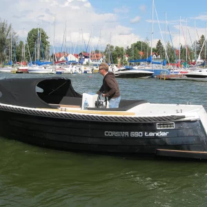 Schwarze Corsiva 690 Tender mit Verdeck und großer Badeplattform bei der Fahrt durch einen Yachthafen.